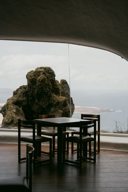 View of a dining table by a window with rock formations and ocean in background.