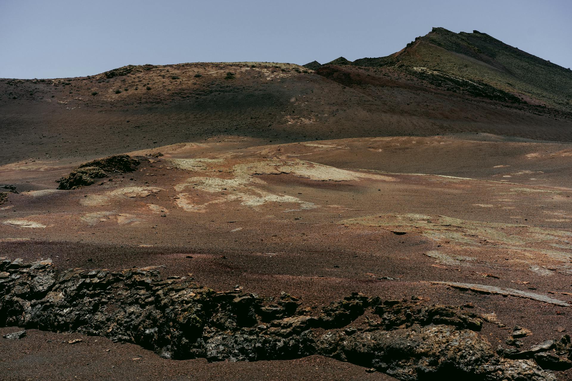 A vast barren landscape showing volcanic terrain and sulfur deposits under a clear sky.