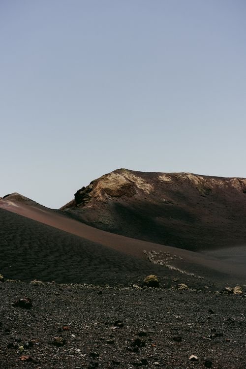Free Dramatic view of a barren volcanic landscape featuring a rugged hill and dark soil under a clear sky. Stock Photo