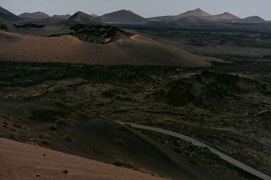 A sweeping aerial view of a stark volcanic landscape with barren terrain and distant mountains.