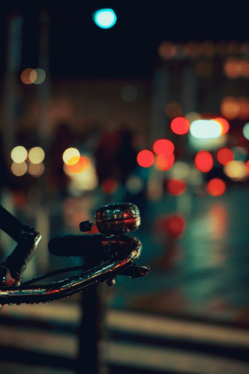 Free Close-up of bicycle handlebars with raindrops in a vibrant city night setting with bokeh lights. Stock Photo