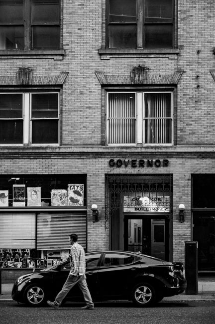 Man walking past a parked car and brick building in urban setting.
