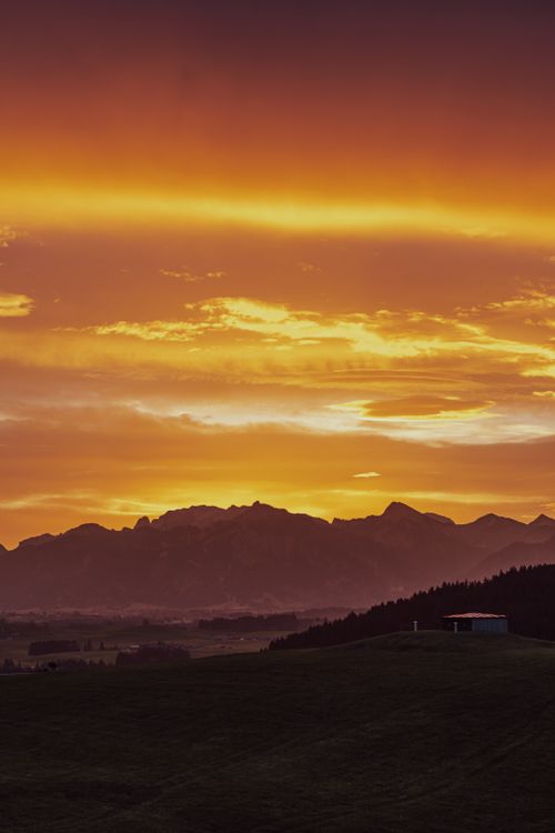 Free A breathtaking sunset over a silhouetted mountain range with vibrant clouds. Stock Photo