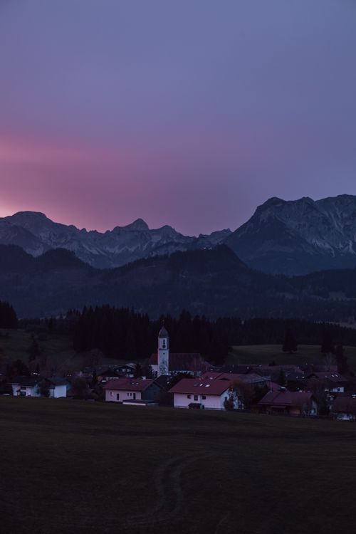 Free Picturesque village nestled beneath mountains at twilight with a church in view. Stock Photo
