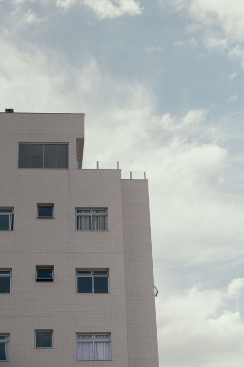 Free A minimalist view of a white building facade with glass windows set against a cloudy sky. Stock Photo
