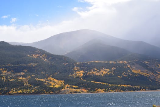 在清澈的蓝天下，宁静的山地景观、风景如画的湖泊和充满活力的秋叶构成了一幅美丽的画卷