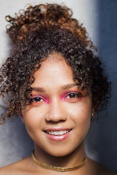 Close-up headshot of a young woman with curly hair and vibrant makeup, smiling warmly.