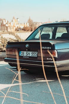 Vintage BMW 325i parked on asphalt road in Türkiye, showcasing car's rear design.