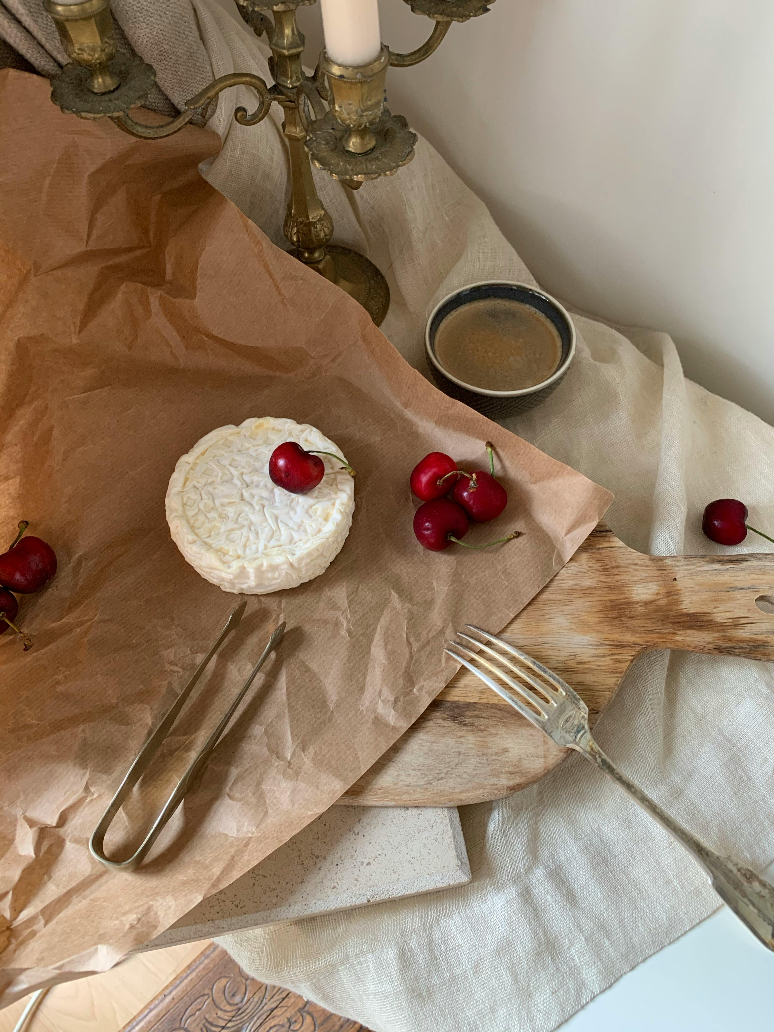 Simple and elegant still life image featuring camembert cheese and cherries on a rustic table setting.