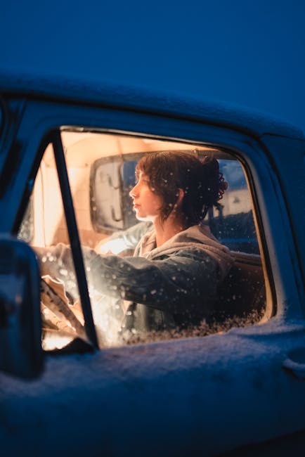 Young woman drives a pickup truck on a snowy winter evening, illuminated interior with cold blue tones.