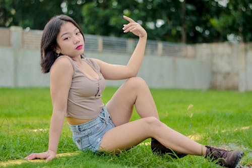 Young Woman in Brown Crop Top and Blue Denim Shorts Sitting on Green Grass