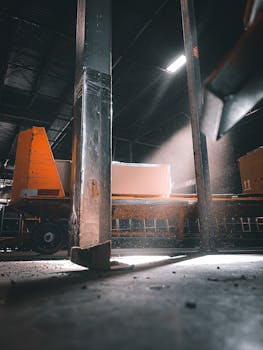 Sunlight streaming through warehouse beams onto industrial equipment in a factory setting.