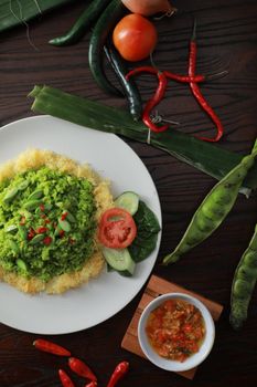Close-up of Nasi Uduk garnished with fresh vegetables and spicy sambal on a wooden table. - Fotografer Sidoarjo