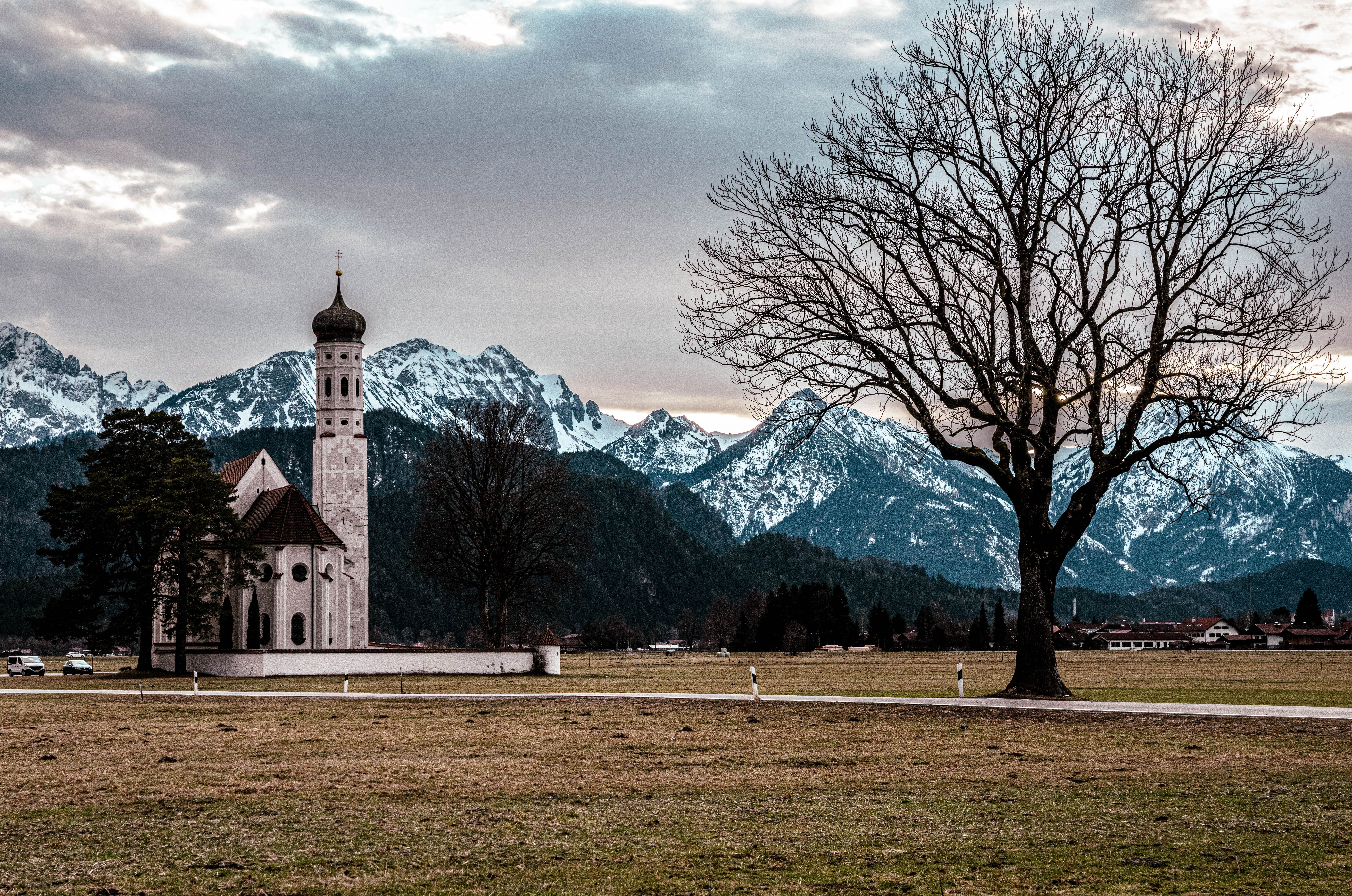 St. Coloman Church near snowy Bavarian Alps in Schwangau, Germany, under a cloudy sky.