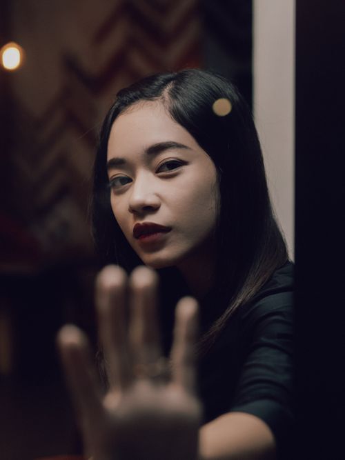 Free A thoughtful Asian woman with dark hair gazing through a window, captured in a low-light setting. Stock Photo