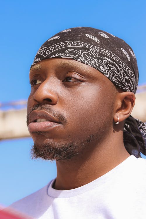 Photo of a Young Man in a White T-shirt and a Bandana Standing Outside 