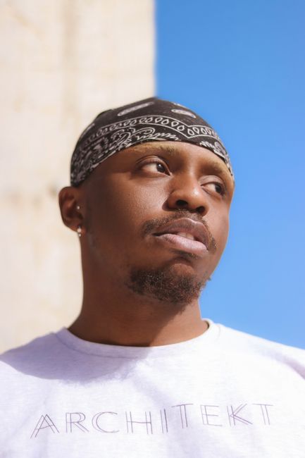 Close-up portrait of a man wearing a bandana under a clear blue sky, looking thoughtfully away.
