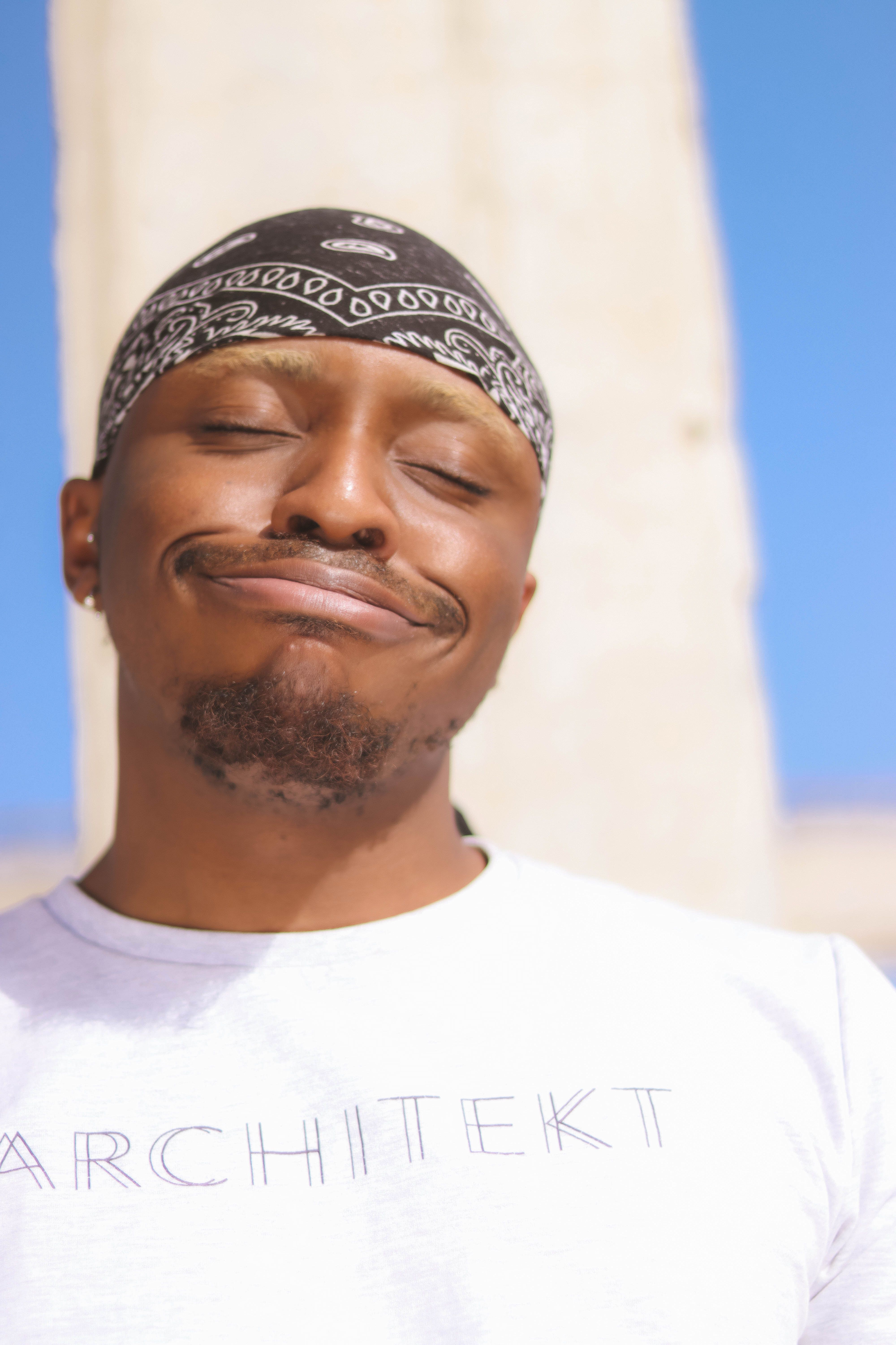 Smiling man enjoying outdoors, wearing bandana and white t-shirt, showcasing fun demeanor.