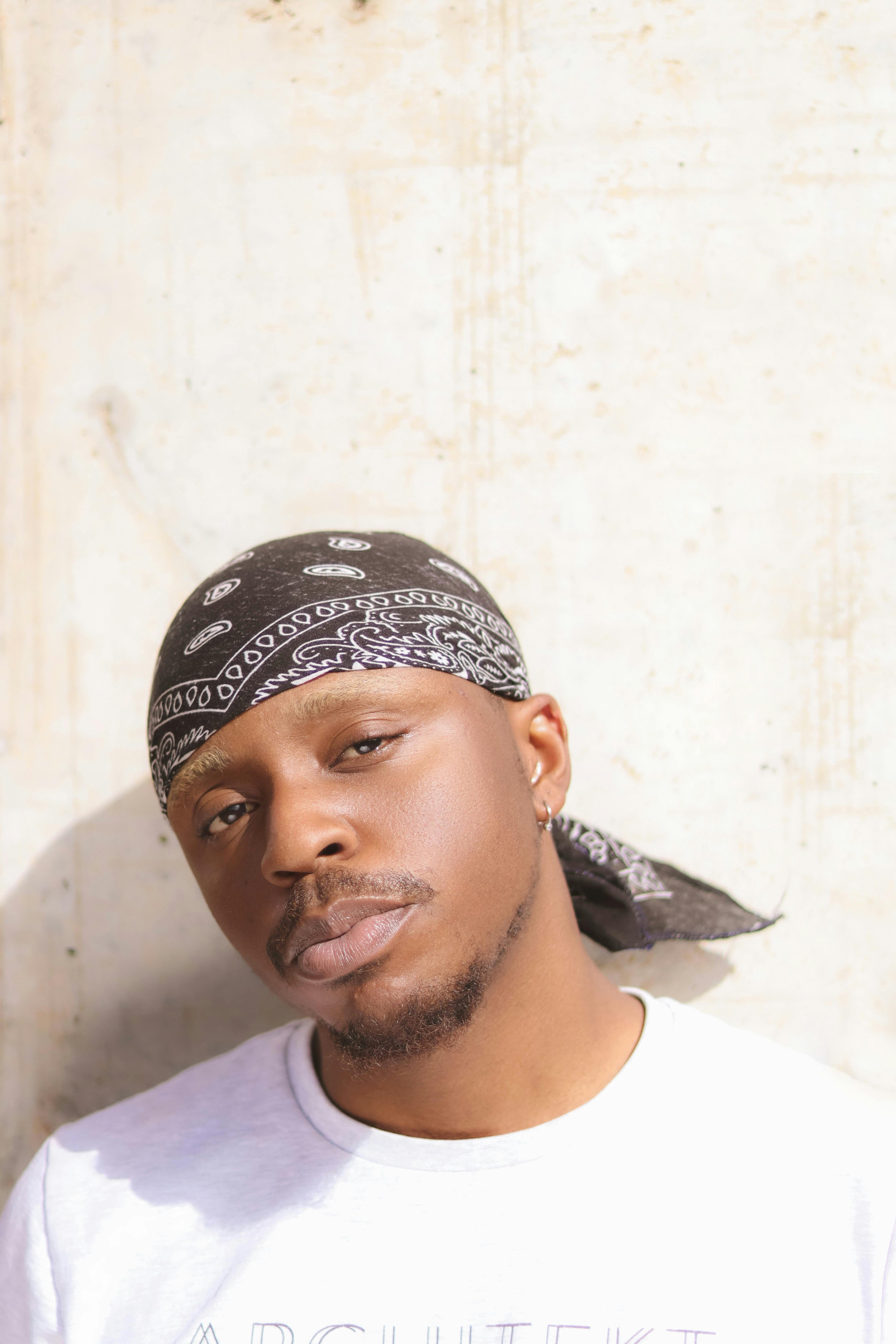 Portrait of a stylish man wearing a bandana, photographed in natural light against a textured wall.