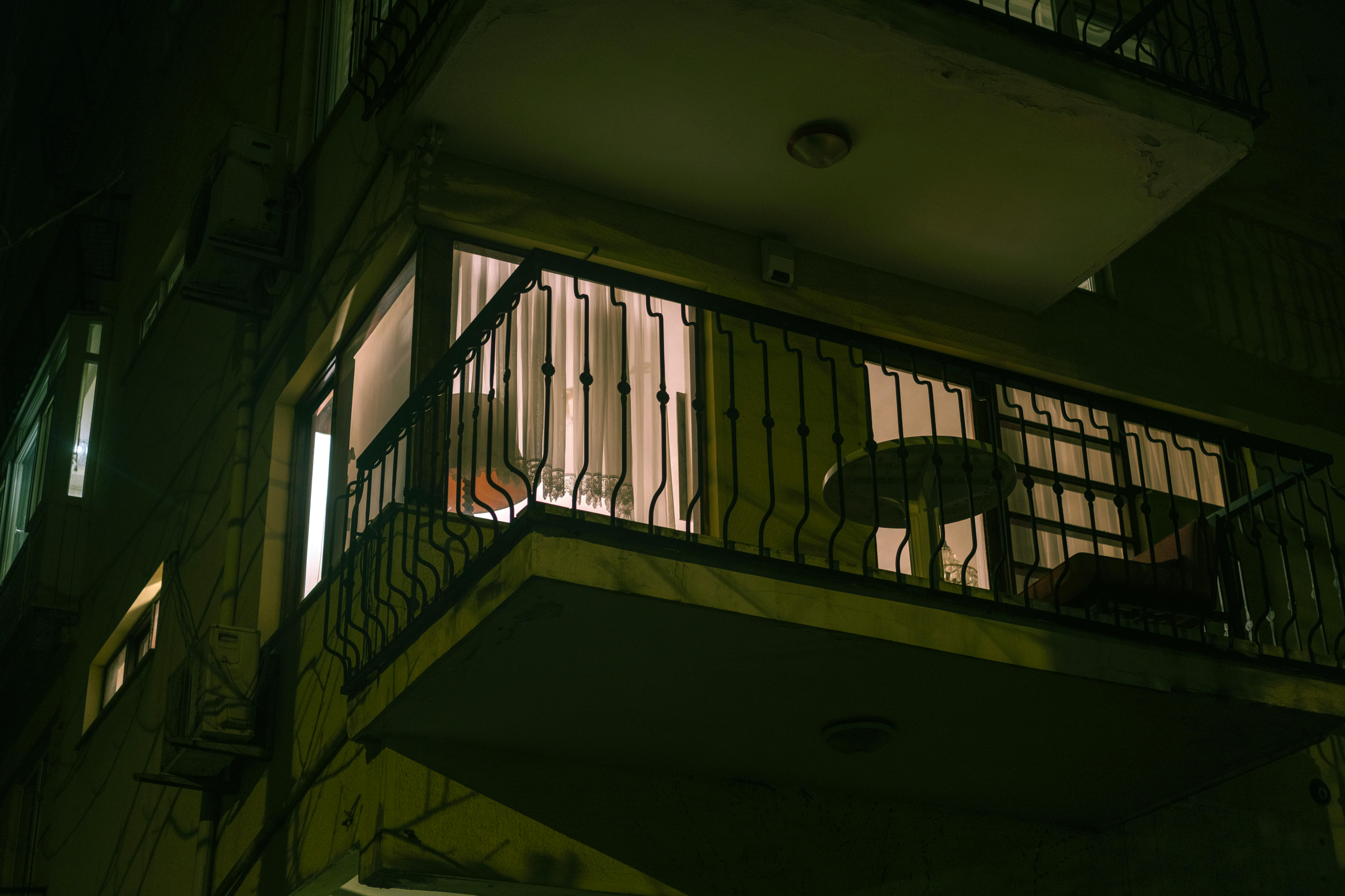A dimly lit urban balcony with chairs and a table at night, creating a moody atmosphere.