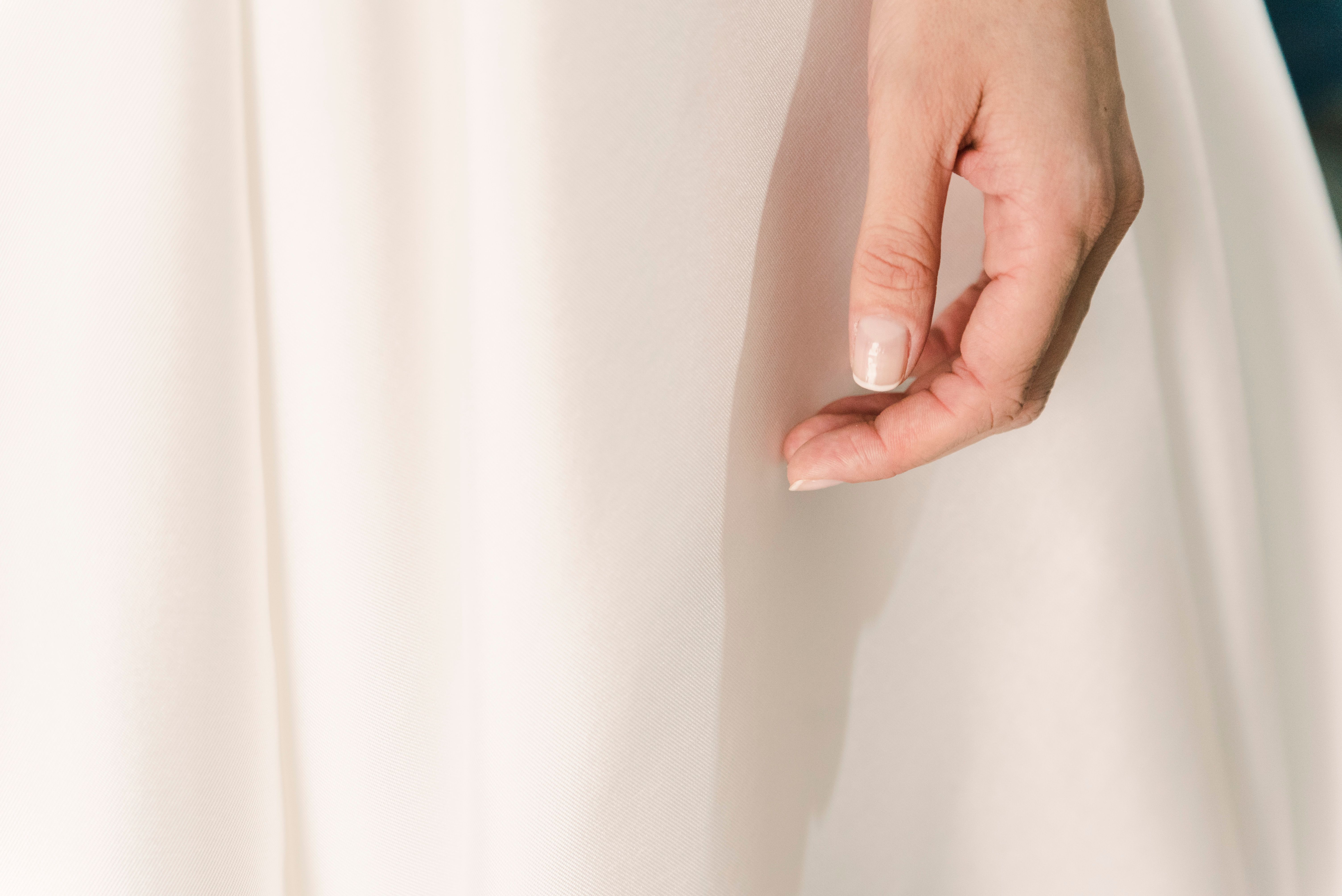 Detailed close-up of a woman's hand resting on a white dress, highlighting elegance and fashion.