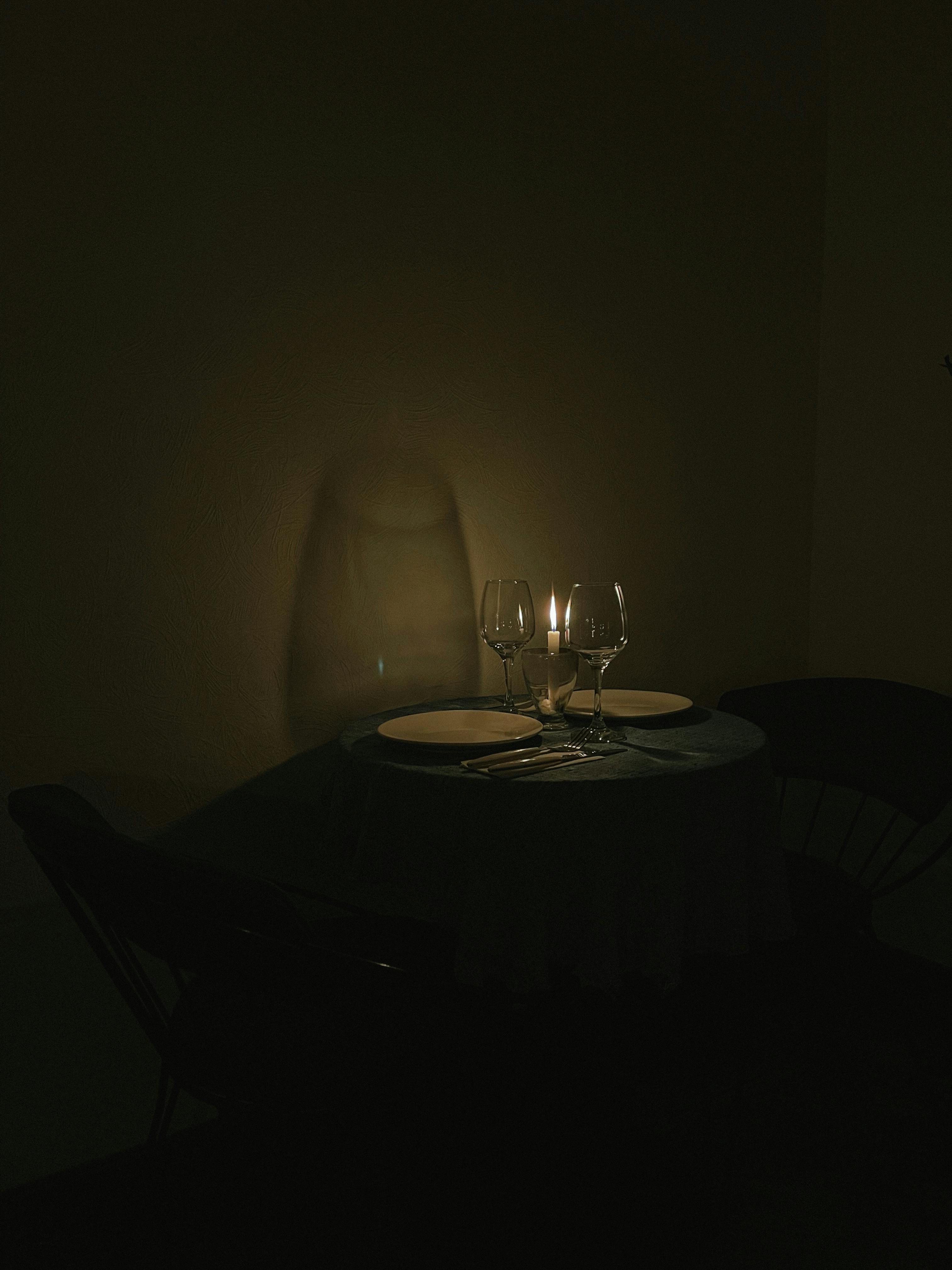 Elegant candlelit dinner setting with wine glasses and plates on a table, creating a cozy ambiance.