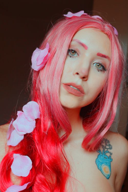 Free A striking portrait of a woman with pink hair adorned with petals, showcasing vibrant colors and artistic makeup. Stock Photo