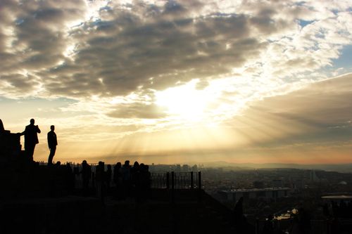 Free Silhouette of people standing against a dramatic skyline and sunset, with rays of light streaming through clouds. Stock Photo
