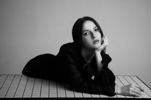 A Grayscale Photo of a Woman in Black Long Sleeves Dress with Her Hand on Her Chin