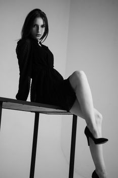 Black and white portrait of a woman in a black dress posing elegantly indoors.
