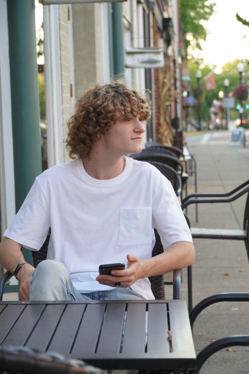 Free Young man with smartphone sitting at outdoor cafe in Marietta, OH, relaxing on a summer day. Stock Photo