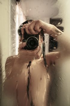 A photographer captures an artistic mirror selfie in a humid bathroom with a vintage camera effect.