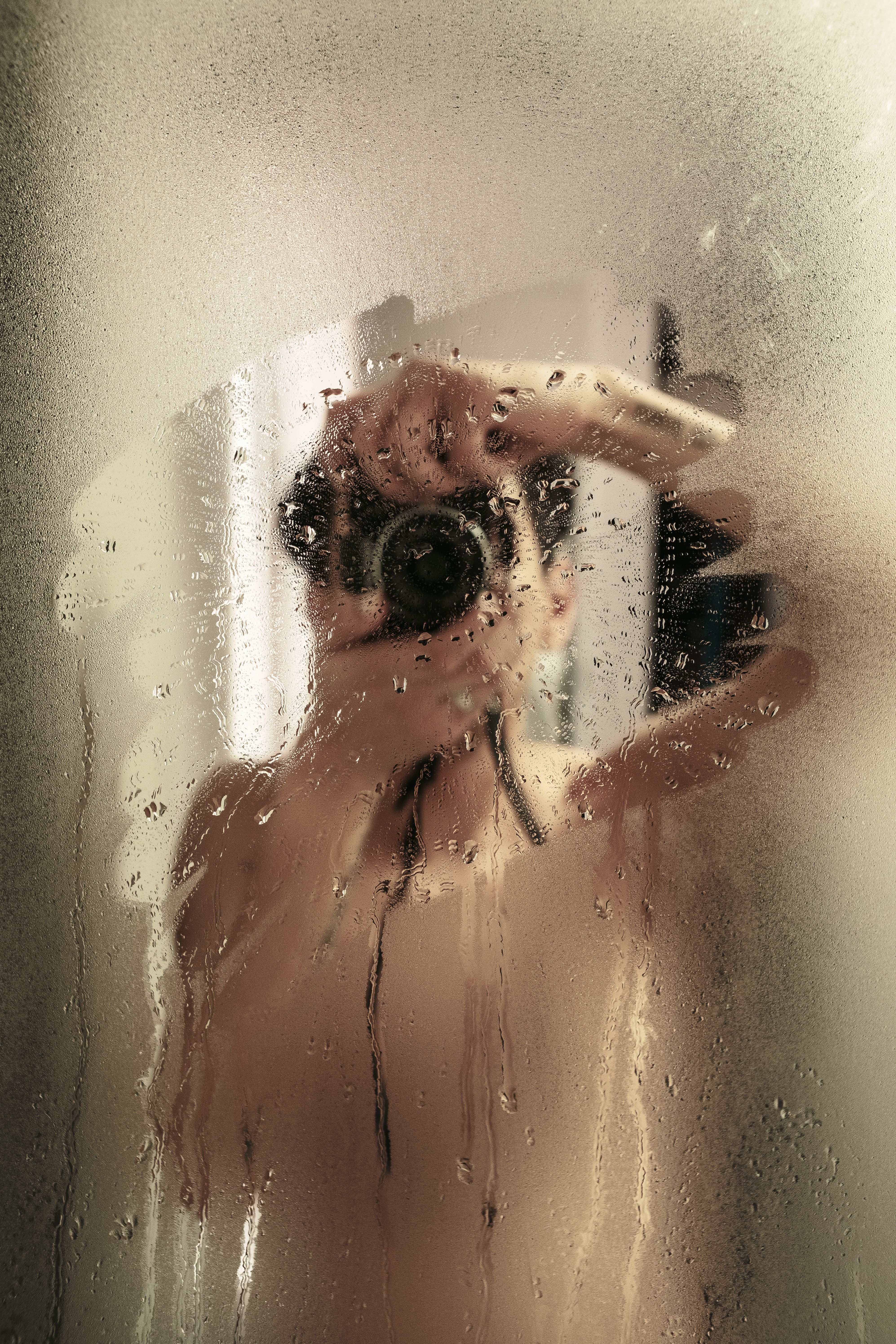 Artistic shot of a person taking a photograph through a steamy bathroom mirror.