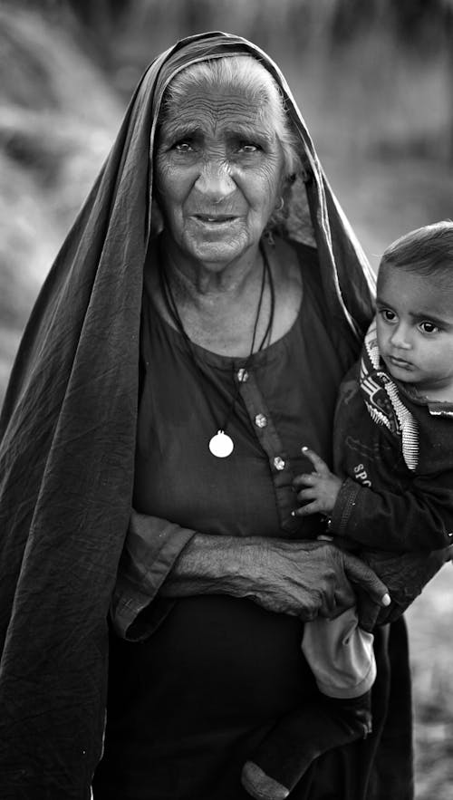 An Old Woman with Headscarf Carrying a Child