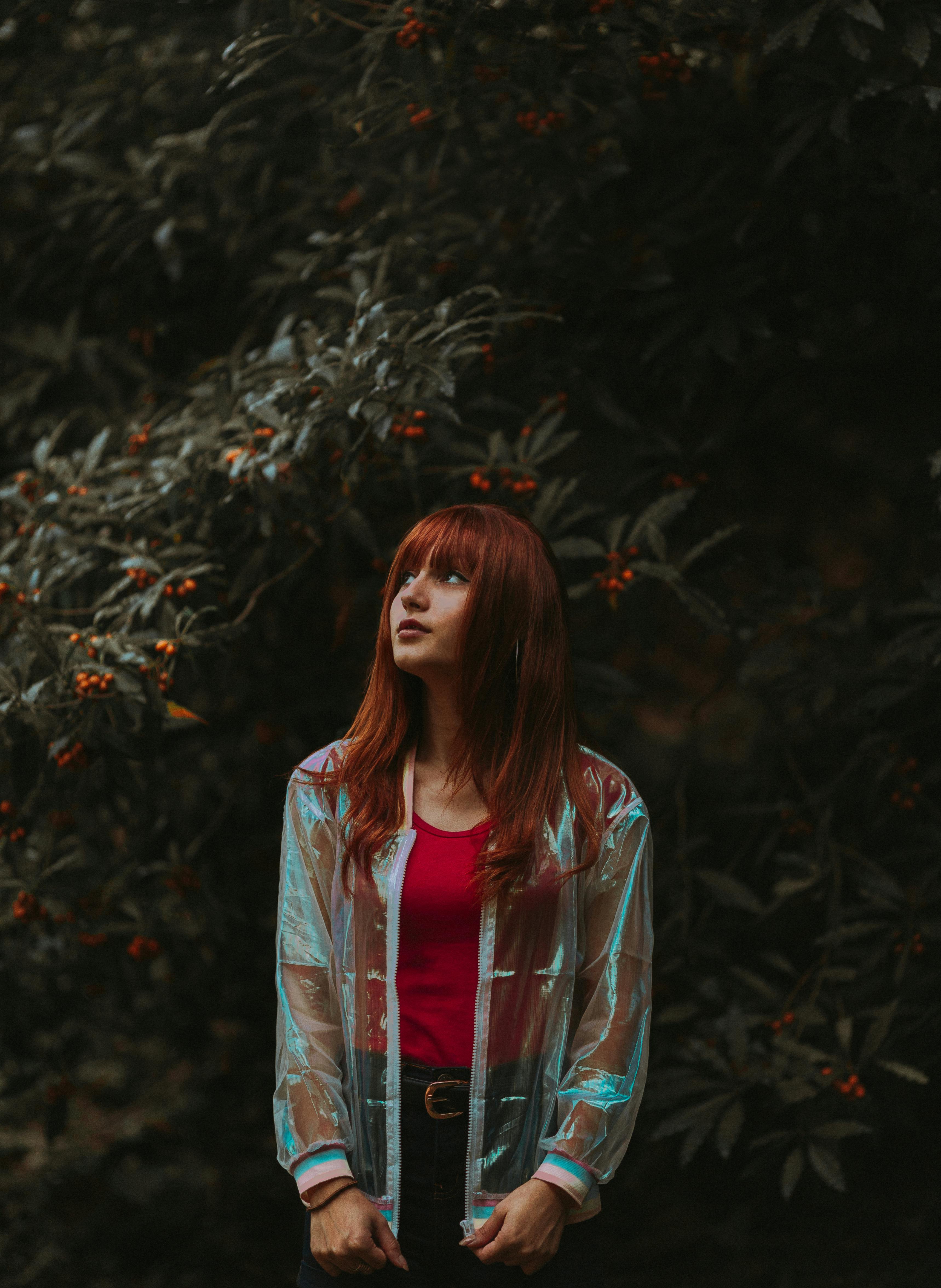 一名年轻女子站在郁郁葱葱的树叶和浆果间，若有所思