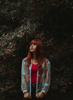 一名年轻女子站在郁郁葱葱的树叶和浆果间，若有所思