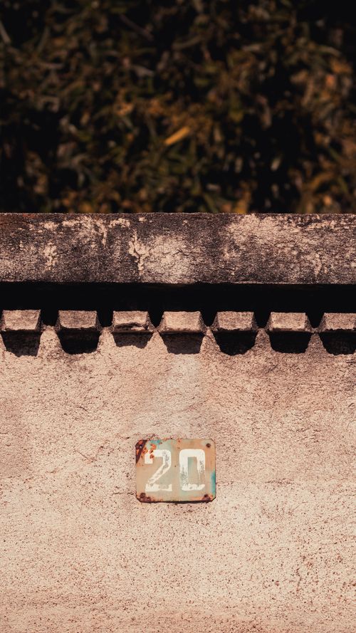 Free Close-up of a sunlit rustic wall featuring an aged number 20 sign, perfect for residential themes. Stock Photo