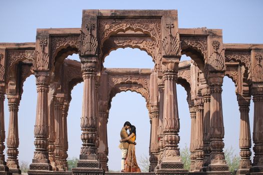 Couple embracing under ancient stone arches in Jodhpur, India against a clear blue sky.