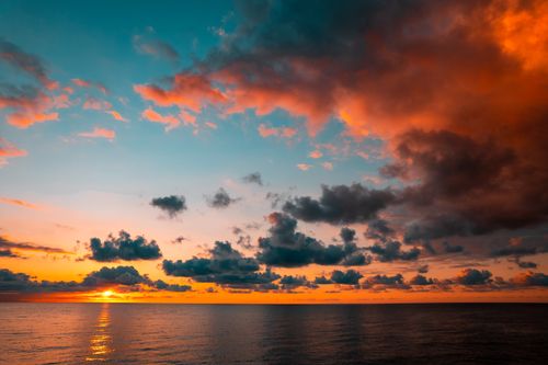 Free Stunning ocean sunset with vibrant clouds and reflections on the water. Stock Photo