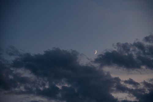 Free A serene view of a crescent moon amidst clouds during evening twilight. Stock Photo