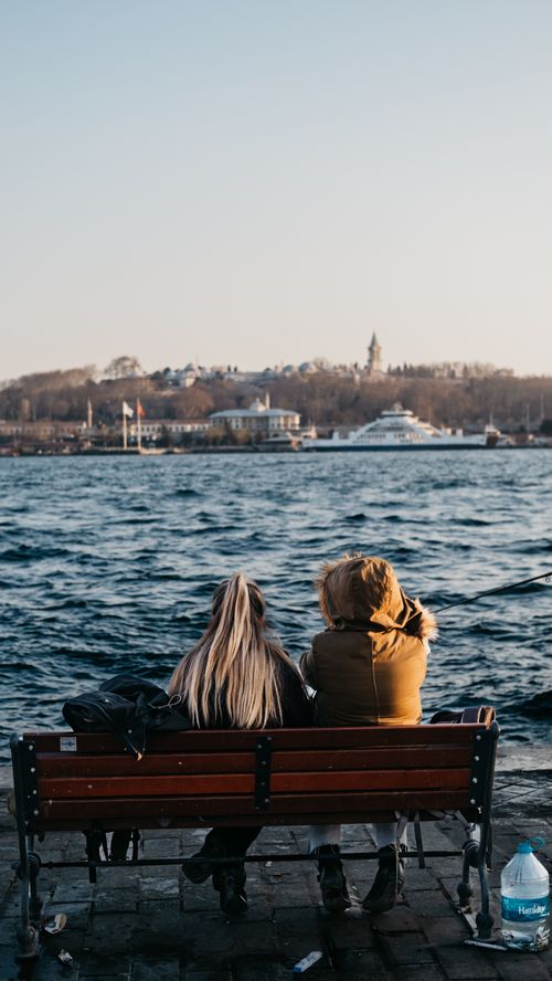 Free Two women sit on a bench enjoying the waterfront view of the Bosphorus in Istanbul, Turkey. Stock Photo