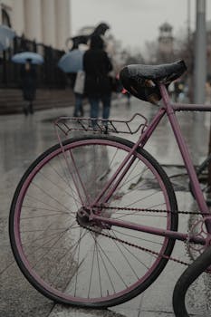 A close-up of a pink bicycle against a wet city street backdrop, captured on a rainy day.