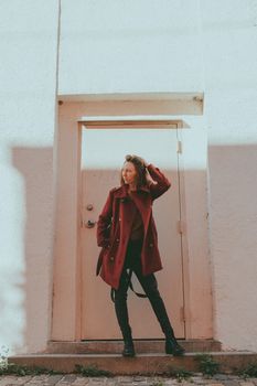 Fashionable woman in a red coat poses confidently against a light-colored door.