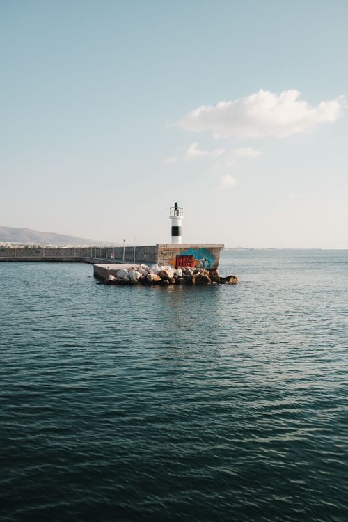 Free A serene view of a lighthouse on a small rocky island by the sea under a clear sky. Stock Photo