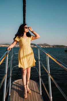 A woman in a yellow dress stands confidently on a sailboat, enjoying a sunny day.