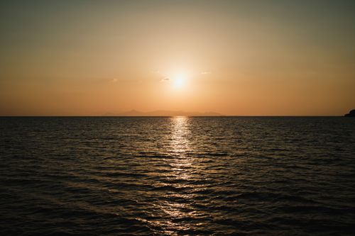 Free A tranquil scene of a sunset over the calm sea, casting a golden glow across the water. Stock Photo