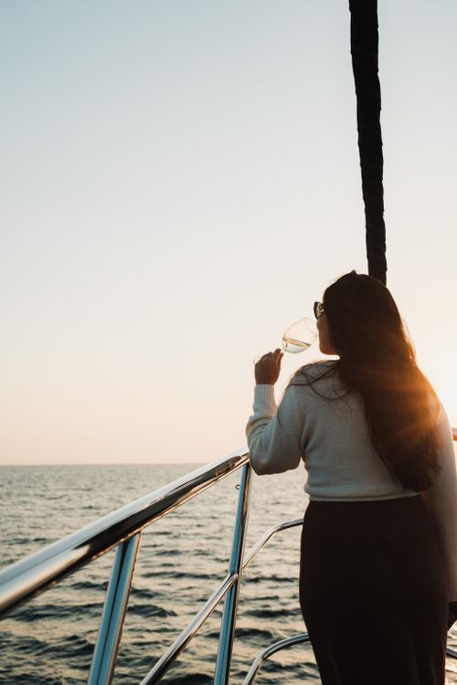 Free A woman stands on a yacht deck, sipping wine and enjoying the sunset over the ocean. Stock Photo