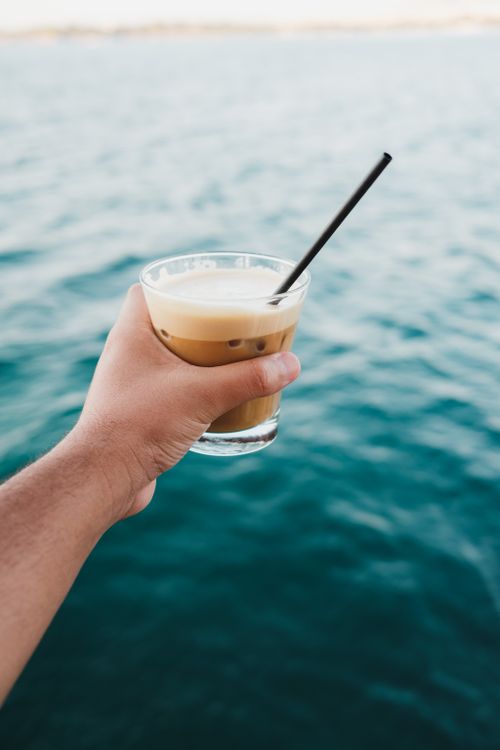 Free Refreshing iced coffee held over the ocean, perfect summer vibe. Stock Photo