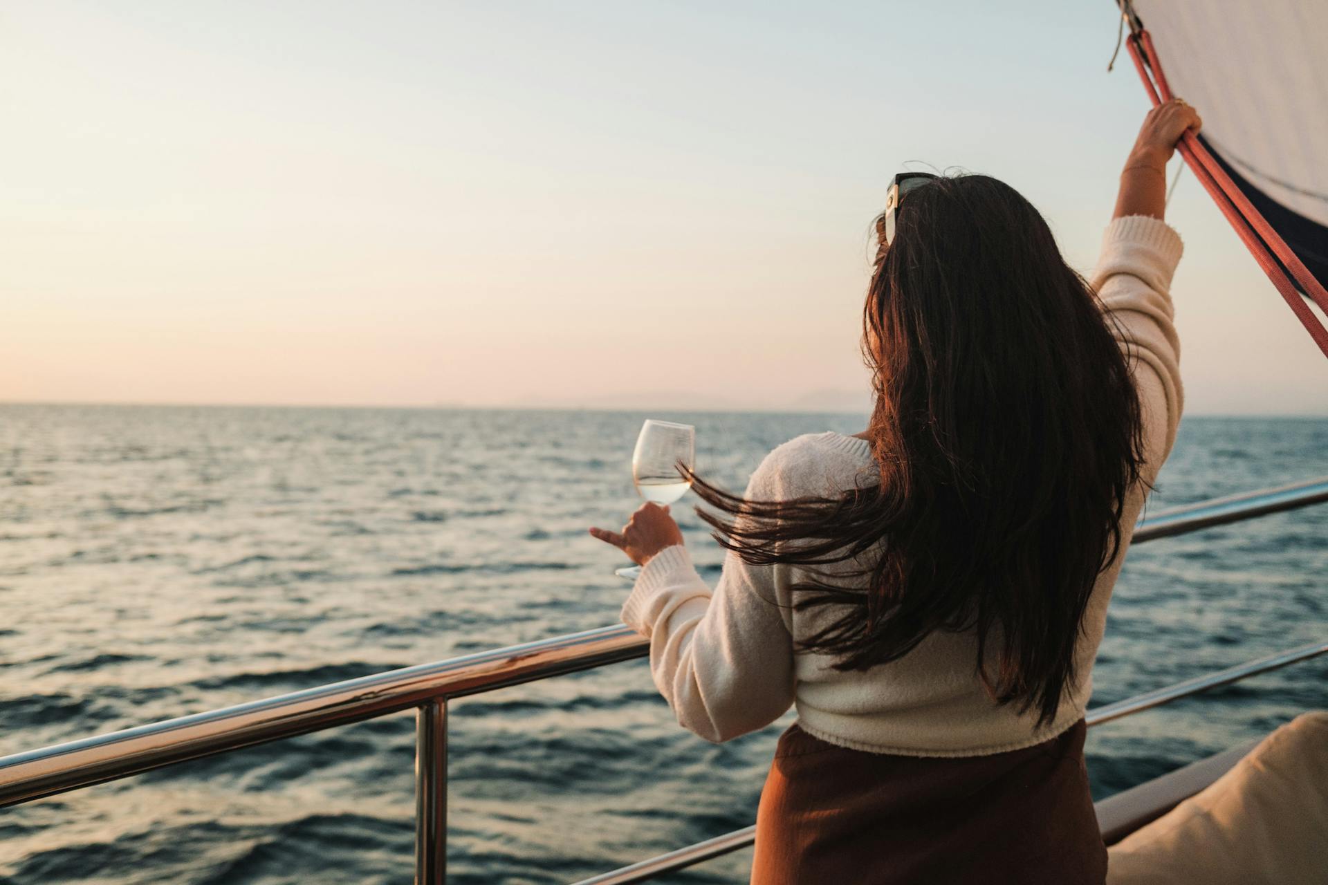 A woman with long brunette hair enjoys a drink while sailing at sunset.