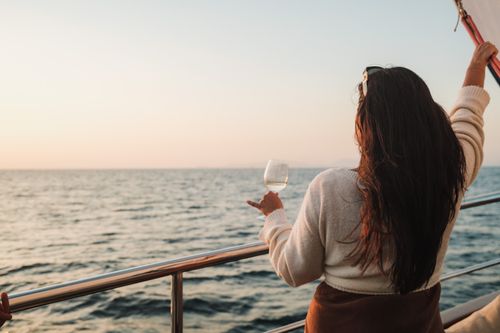 Free A woman with long hair holds a drink on a sailboat, enjoying a sunset view at sea. Stock Photo